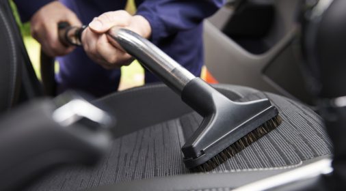 Man hoovering seat of a car during cleaning