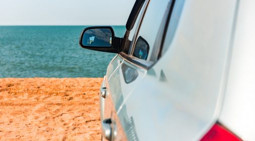 The left of a silver car on a beach with the sand and sea in the background