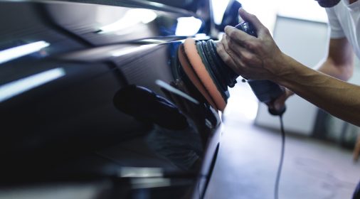 Hands with orbital polisher in auto repair shop. Selective focus.