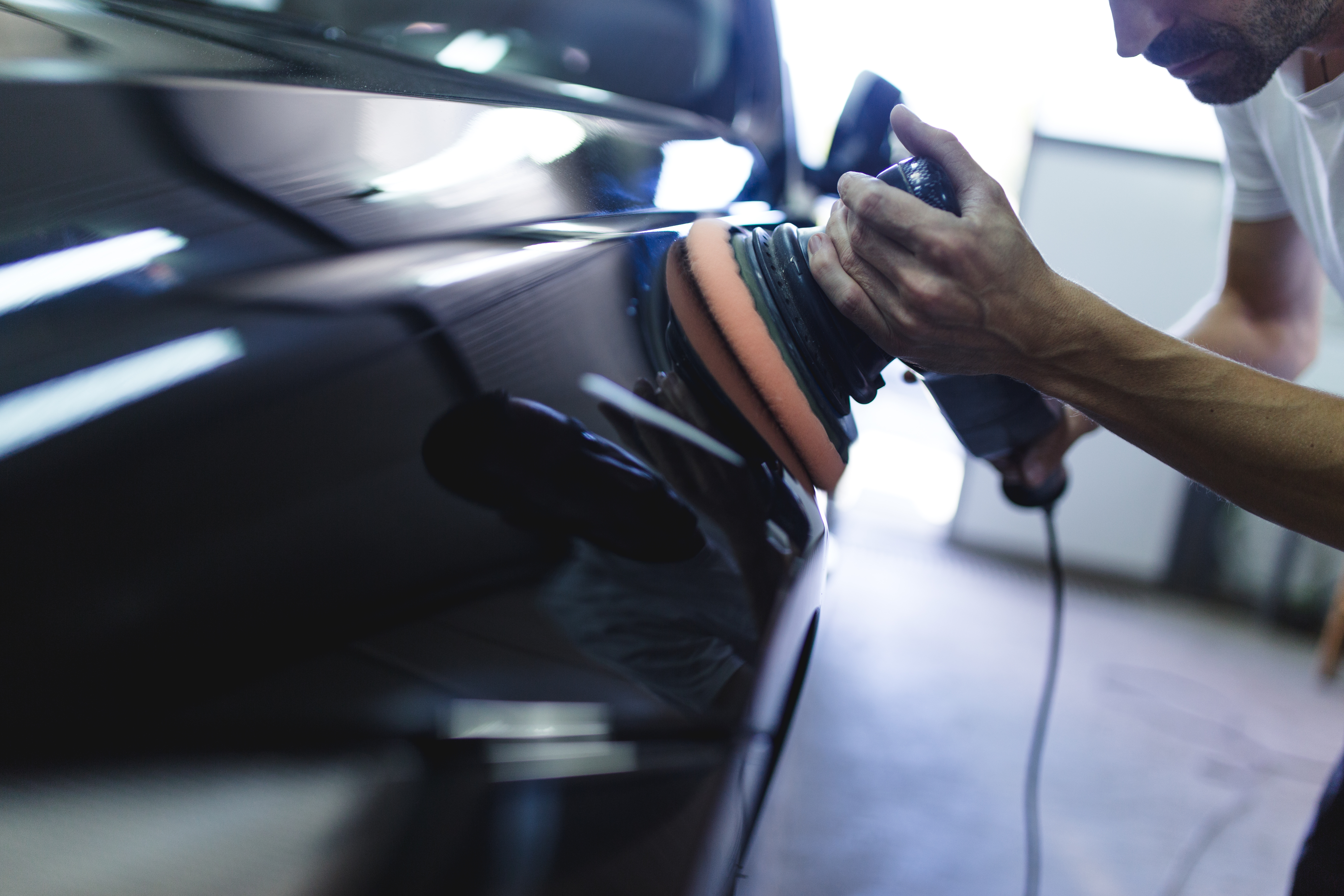 Hands with orbital polisher in auto repair shop. Selective focus.