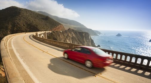 red car driving abroad next to the sea