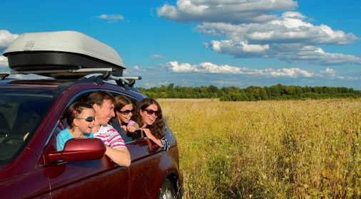 a family sat in a car leaning out of car window in a field