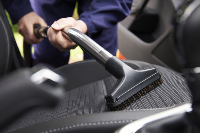 Man hoovering seat of car during car cleaning