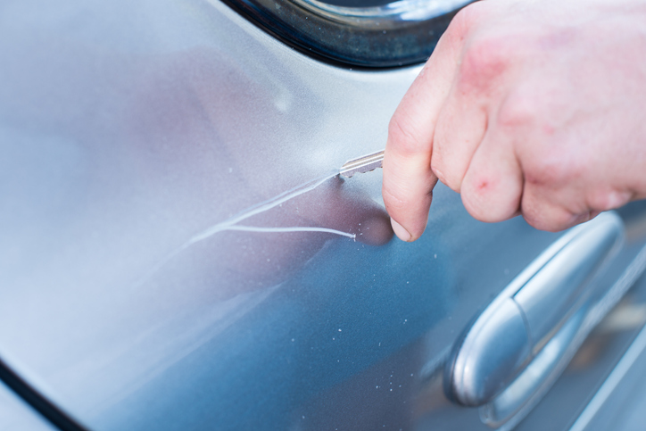 Man's hand scratching a car with a key.