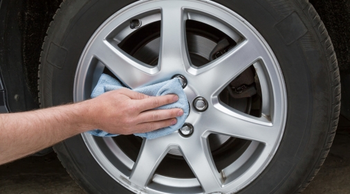 Man's hand with rag cleaning a dusty car wheel disk in the garage. Early spring washing or regular wash up. Professional car wash by hands.