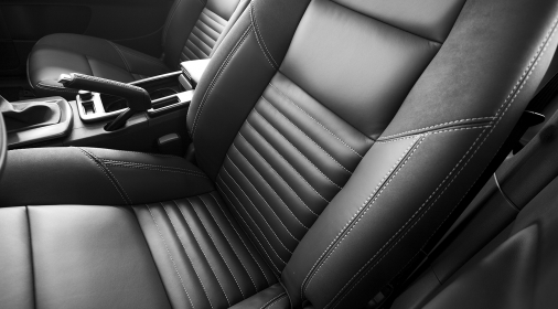 A black leather driver's and passenger's seat of a vehicle. The two seats are divided by a center console with the emergency brake visible. The driver's seat is positioned a bit further forward than the passenger's seat. The seats are stitched with white thread.