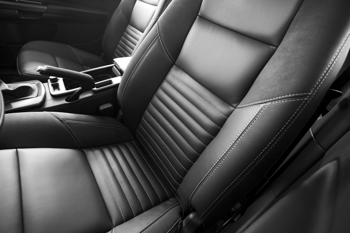 A black leather driver's and passenger's seat of a vehicle. The two seats are divided by a center console with the emergency brake visible. The driver's seat is positioned a bit further forward than the passenger's seat. The seats are stitched with white thread.