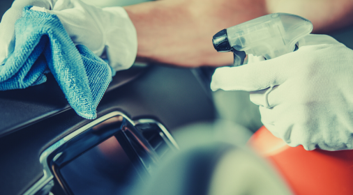 Hands in gloves using spray and cloth to clean car interior