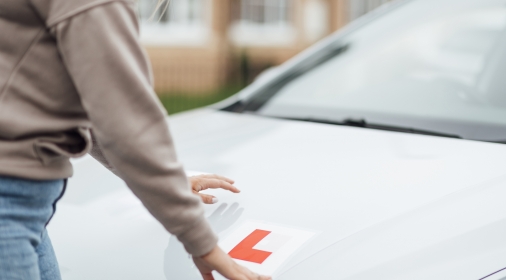 A shot of a Caucasian female putting L Plates on her car ready for her driving lesson.