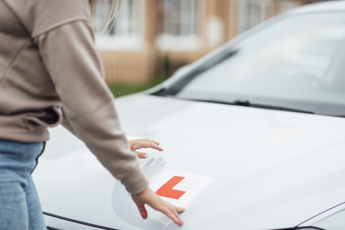 A shot of a Caucasian female putting L Plates on her car ready for her driving lesson.