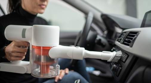 Young woman sitting in car and cleaning car dashboard with hand vacuum cleaner